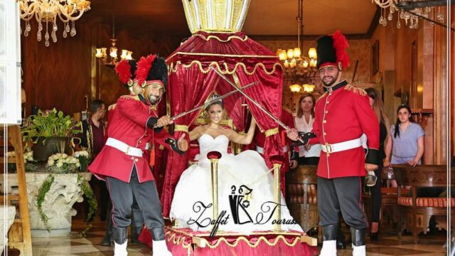 a woman in a white dress with a crown and a couple men in red uniforms